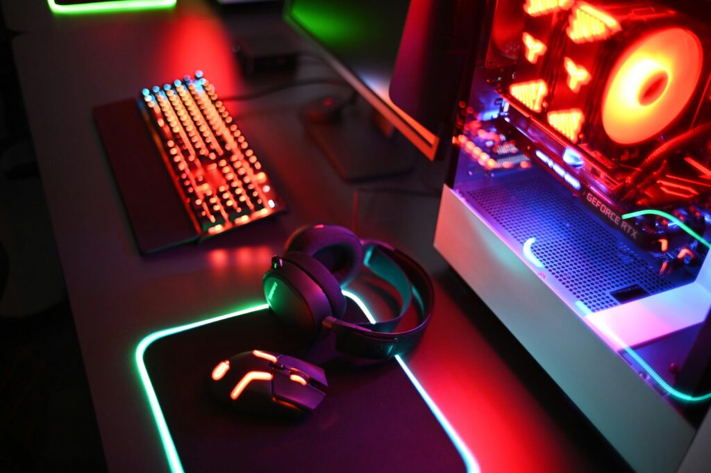 A colorful, vivid image of a desktop with a pc on it, a mousemat, mouse, headphones and keboard. The peripherals are black with RBG turned on.