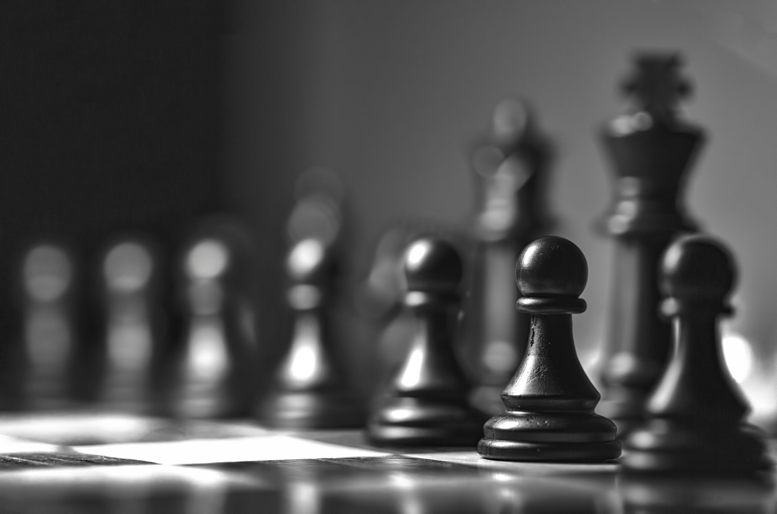 Closeup of the black pawn pieces in front of some blurry other chess pieces.
