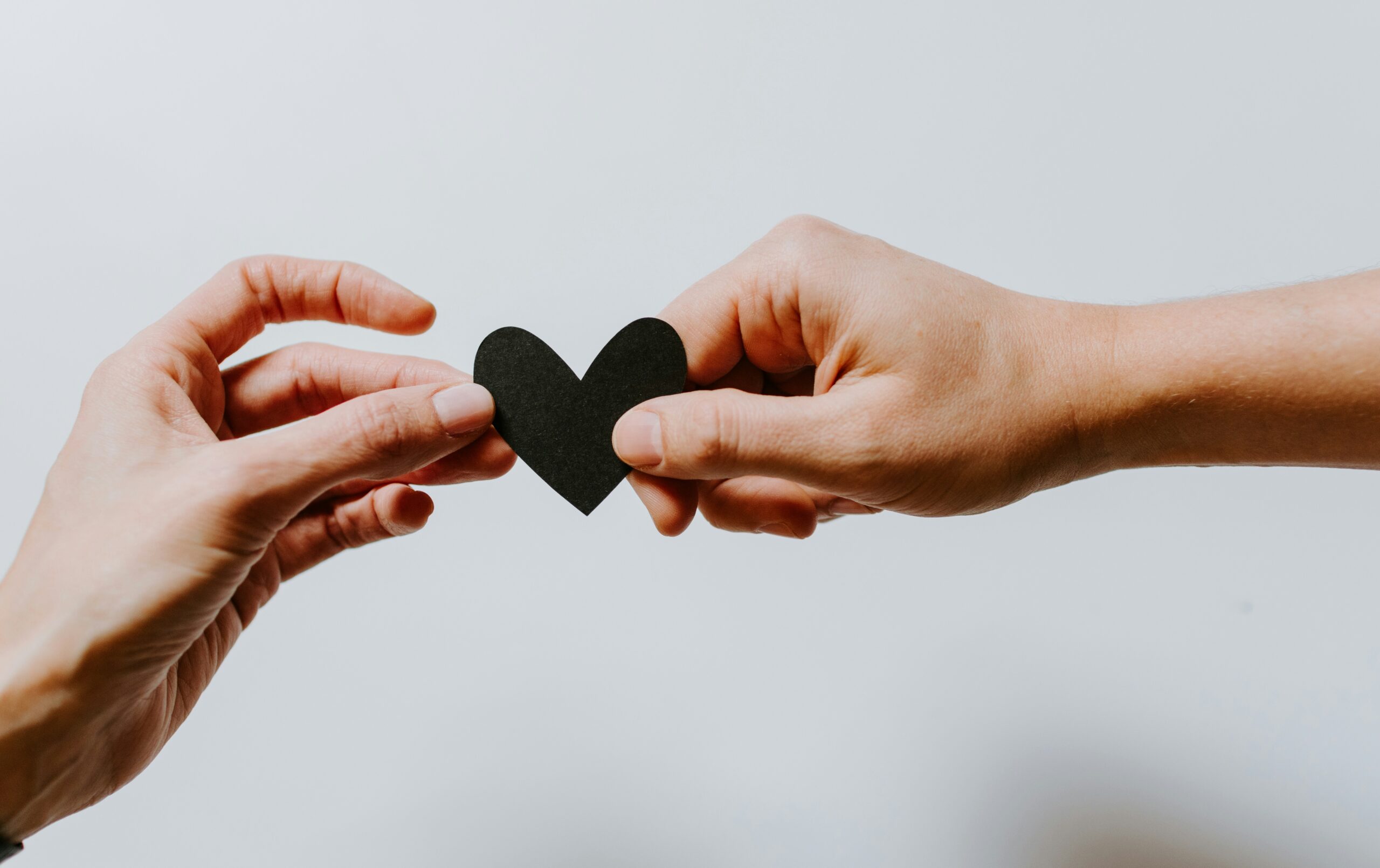 Two hands holding a black paper cutout of a heart in front of a white background